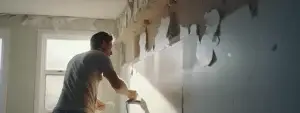 a person repairing damaged drywall with a putty knife and patching compound.